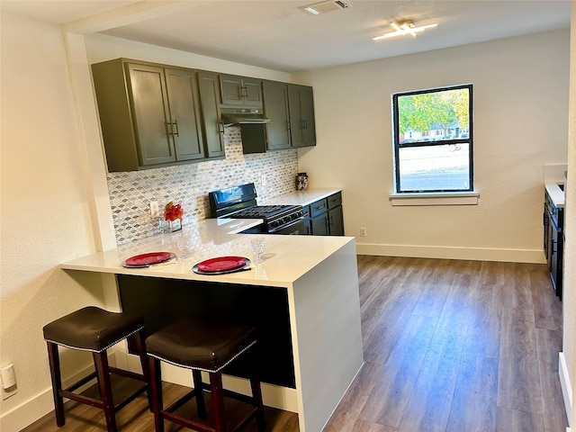 kitchen with decorative backsplash, a breakfast bar area, hardwood / wood-style floors, and black range oven