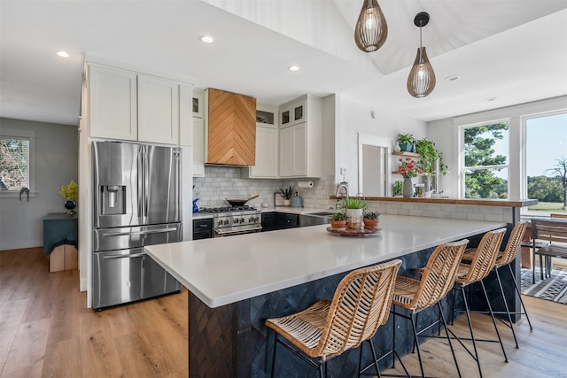 kitchen featuring tasteful backsplash, light hardwood / wood-style floors, white cabinetry, appliances with stainless steel finishes, and decorative light fixtures