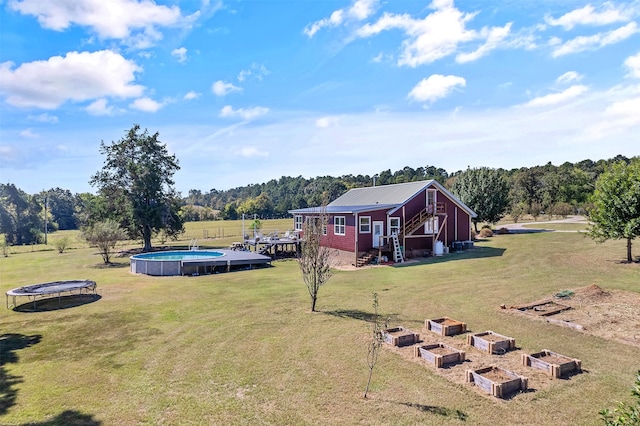 view of yard with an outdoor pool, a trampoline, and a vegetable garden