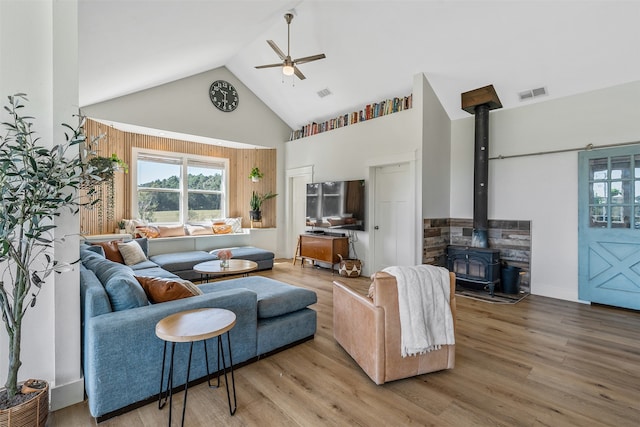 living room with wood-type flooring, a wood stove, high vaulted ceiling, and ceiling fan