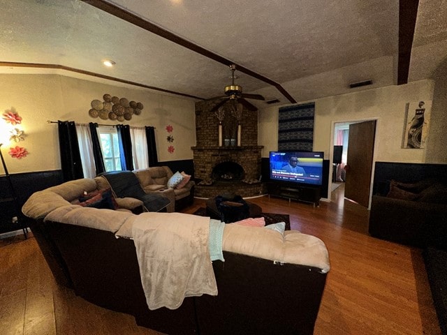 living room with ceiling fan, hardwood / wood-style floors, a textured ceiling, and a brick fireplace