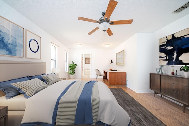 bedroom with wood finished floors, a textured ceiling, ceiling fan, baseboards, and visible vents
