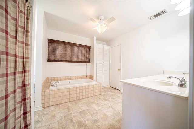 bathroom featuring ceiling fan, tiled tub, and vanity