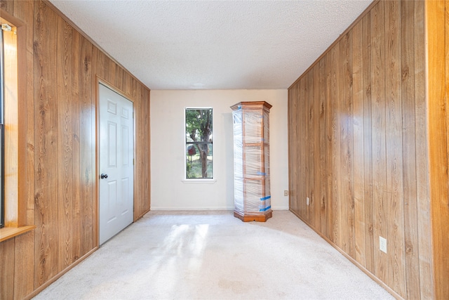 empty room featuring a textured ceiling, wooden walls, and light carpet