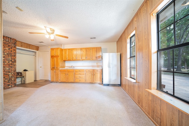 kitchen with ceiling fan, light carpet, wooden walls, white fridge, and a textured ceiling