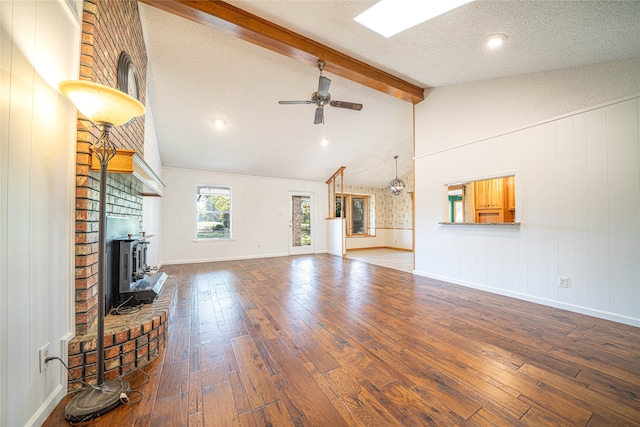 unfurnished living room featuring hardwood / wood-style flooring, vaulted ceiling with beams, a brick fireplace, and a textured ceiling