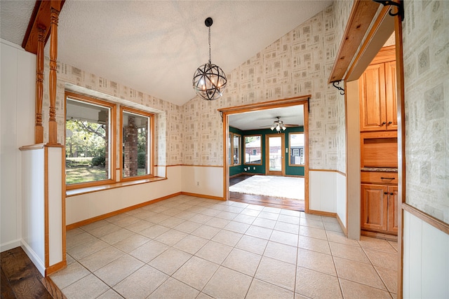 unfurnished dining area with ceiling fan with notable chandelier, vaulted ceiling, light tile patterned floors, and a textured ceiling