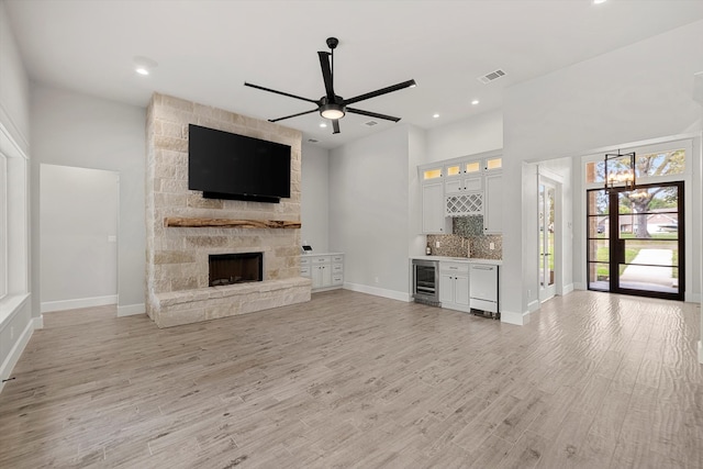 unfurnished living room featuring a fireplace, light hardwood / wood-style floors, bar, ceiling fan, and beverage cooler