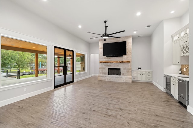 unfurnished living room featuring sink, light wood-type flooring, a fireplace, ceiling fan, and wine cooler