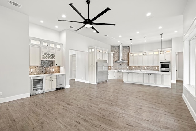 kitchen featuring wall chimney range hood, dark wood-type flooring, wine cooler, decorative light fixtures, and appliances with stainless steel finishes