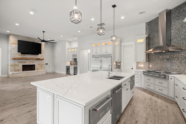 kitchen with a kitchen island with sink, wall chimney range hood, stainless steel appliances, white cabinetry, and light hardwood / wood-style floors