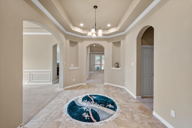 corridor featuring a tray ceiling, light carpet, ornamental molding, and a notable chandelier