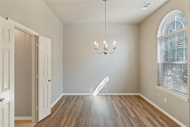 empty room with wood-type flooring and an inviting chandelier