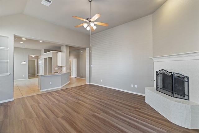 unfurnished living room with a fireplace, lofted ceiling, light wood-type flooring, and ceiling fan