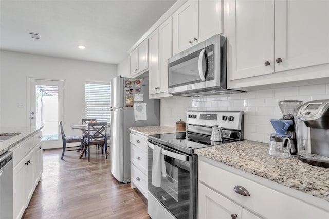 kitchen featuring light stone countertops, tasteful backsplash, appliances with stainless steel finishes, white cabinets, and light wood-type flooring