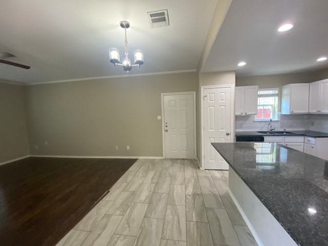 kitchen with white cabinets, hanging light fixtures, sink, dark stone countertops, and crown molding