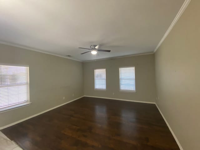 empty room with crown molding, plenty of natural light, and dark wood-type flooring