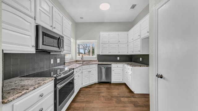 kitchen featuring light stone countertops, visible vents, a sink, dark wood-type flooring, and appliances with stainless steel finishes