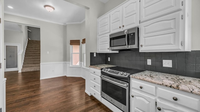 kitchen featuring ornamental molding, light stone counters, dark wood-style floors, stainless steel appliances, and wainscoting