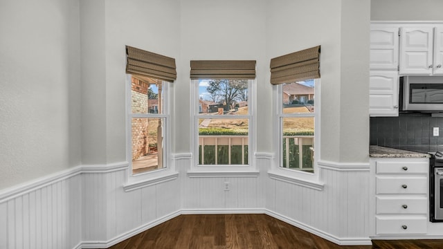 unfurnished dining area featuring dark wood-style floors and wainscoting