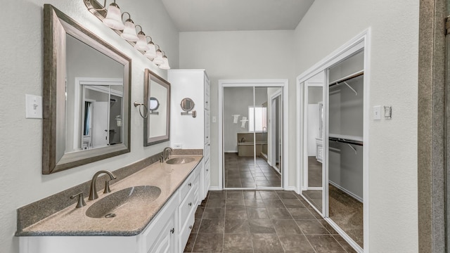 full bath with a sink, baseboards, double vanity, and a spacious closet