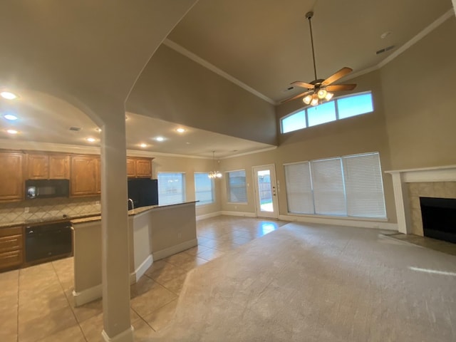 unfurnished living room featuring ceiling fan with notable chandelier, a tiled fireplace, a towering ceiling, ornamental molding, and light tile patterned floors