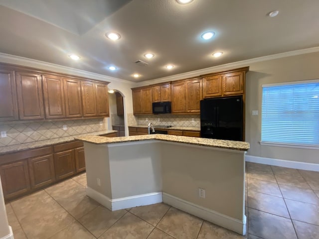 kitchen with a center island with sink, black appliances, decorative backsplash, and light stone counters