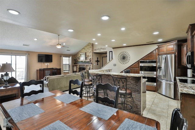 dining area featuring ceiling fan, a large fireplace, lofted ceiling, light tile patterned floors, and a textured ceiling