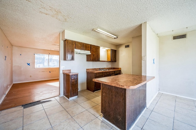 kitchen featuring sink, a textured ceiling, light tile patterned floors, and kitchen peninsula