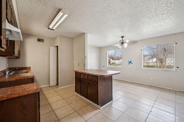 kitchen featuring sink, light tile patterned floors, a kitchen island, ceiling fan, and dark brown cabinetry