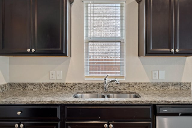 kitchen with stainless steel dishwasher, dark brown cabinets, light stone counters, and a sink