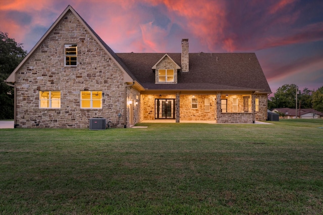 back house at dusk featuring a yard and central AC