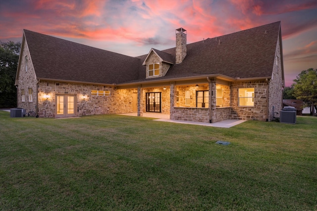 back house at dusk featuring a patio, french doors, a yard, and central air condition unit