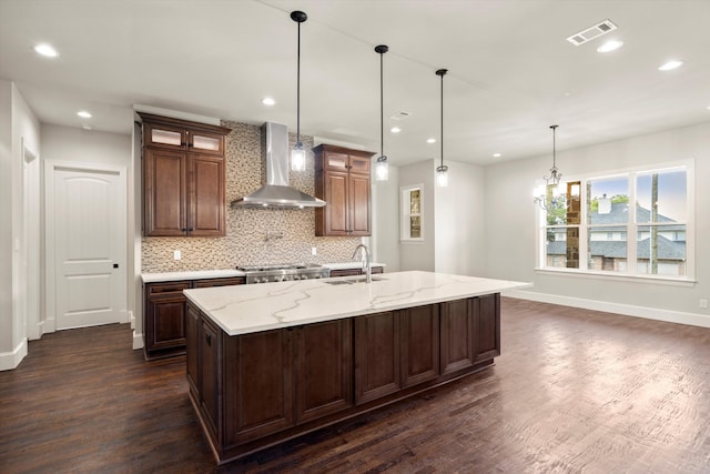 kitchen with wall chimney exhaust hood, sink, an island with sink, and dark hardwood / wood-style floors