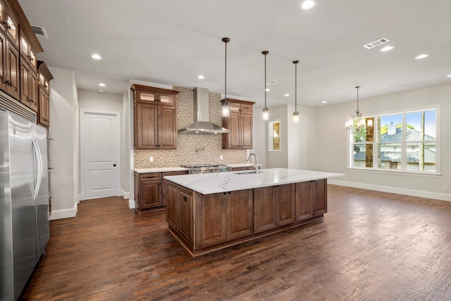 kitchen with a spacious island, wall chimney exhaust hood, appliances with stainless steel finishes, and pendant lighting