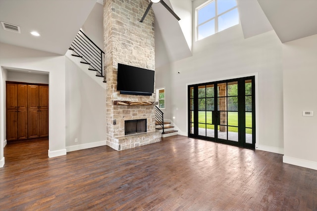 unfurnished living room featuring dark wood-type flooring, a stone fireplace, and a high ceiling