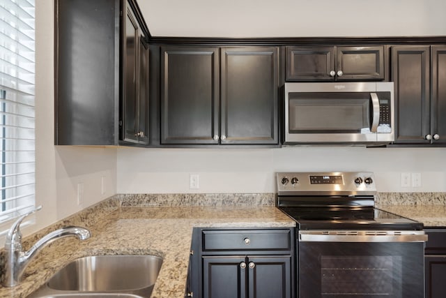 kitchen with appliances with stainless steel finishes, dark brown cabinets, light stone countertops, and sink