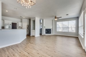 unfurnished living room with ceiling fan with notable chandelier and light hardwood / wood-style floors