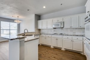 kitchen with white appliances, dark hardwood / wood-style flooring, sink, kitchen peninsula, and white cabinets