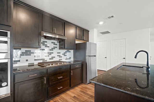 kitchen with dark stone counters, sink, light hardwood / wood-style floors, dark brown cabinetry, and stainless steel appliances