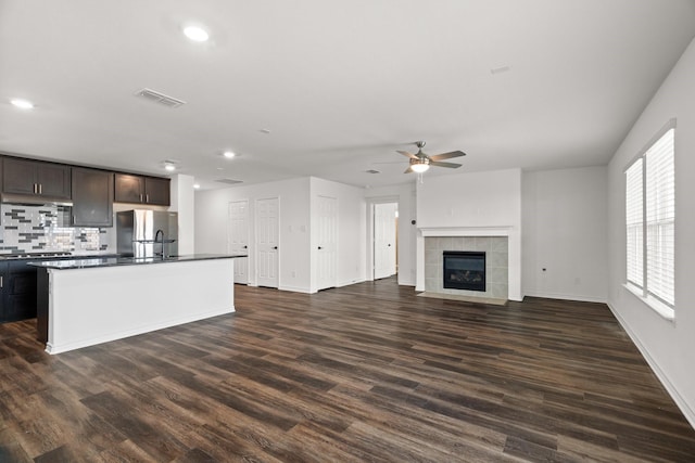 kitchen featuring backsplash, a kitchen island with sink, dark hardwood / wood-style floors, dark brown cabinetry, and stainless steel refrigerator