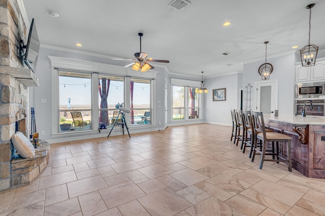 living room featuring a stone fireplace, ceiling fan with notable chandelier, and ornamental molding