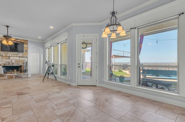 unfurnished dining area with a stone fireplace, ceiling fan with notable chandelier, and crown molding