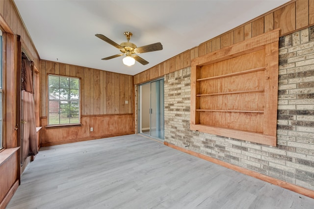 spare room with wood walls, light hardwood / wood-style floors, built in shelves, and ceiling fan