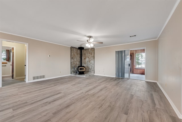 unfurnished living room featuring a wood stove, light wood-type flooring, ceiling fan, and ornamental molding