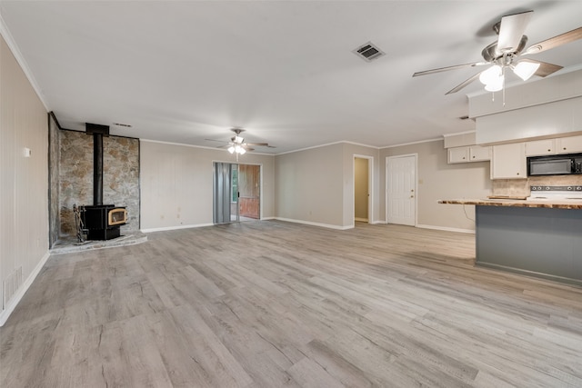 unfurnished living room with ceiling fan, crown molding, light hardwood / wood-style floors, and a wood stove