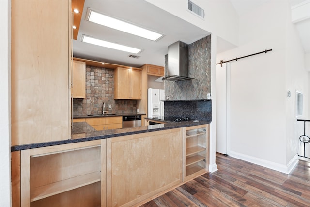 kitchen featuring light brown cabinets, wall chimney exhaust hood, decorative backsplash, a barn door, and dark hardwood / wood-style flooring