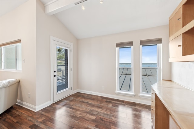 unfurnished dining area featuring vaulted ceiling with beams, a wealth of natural light, a water view, and dark wood-type flooring