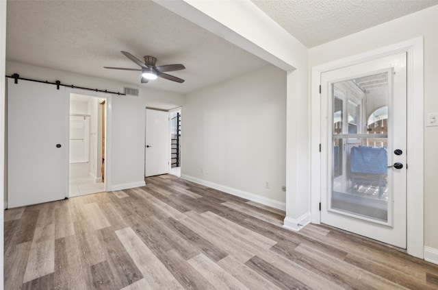 unfurnished room with a textured ceiling, a barn door, light hardwood / wood-style floors, and ceiling fan