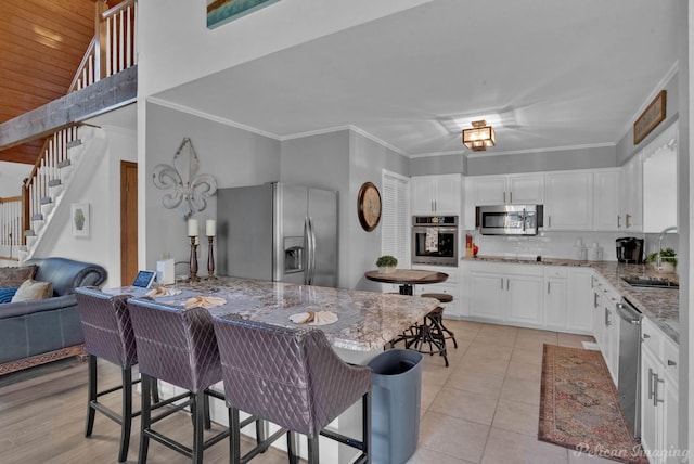 kitchen with appliances with stainless steel finishes, light stone counters, sink, light tile patterned floors, and white cabinetry